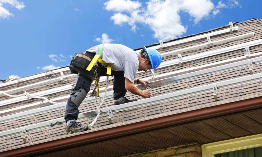 A man installing solar panel rails and hooks on roof