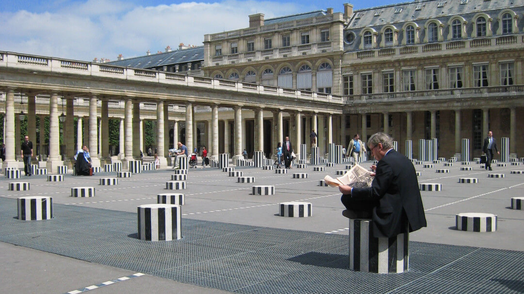 man sitting on Buren columns reading newspaper at Jardins du Palais Royal