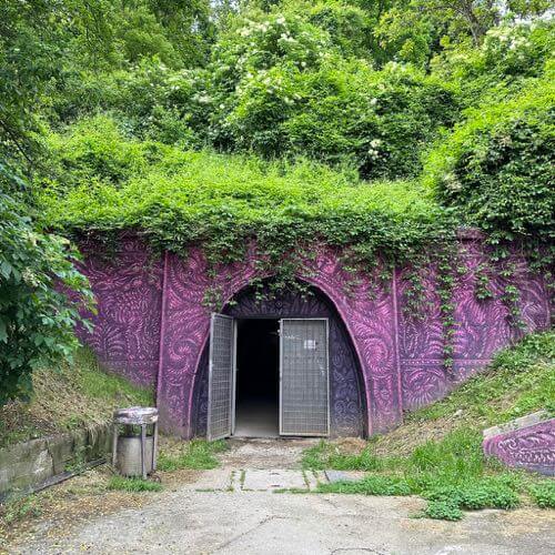 The purple graffiti Tomiceva entrance of Tunel Gric below green trees in Zagreb.