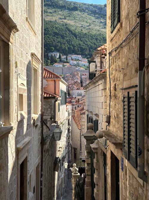 Looking down a narrow lanes between houses of Dubrovnik old town, with tall hillside in the background in Dubrovnik, Croatia