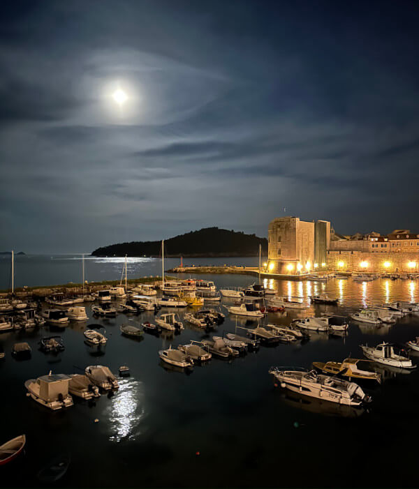 Full moon light shines over the old port of Dubrovnik, Croatia, at night with boats and St Juan Festung Fortress night lights.