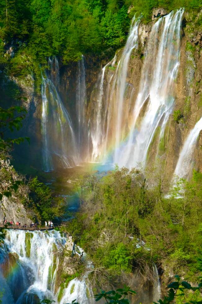 Visitors look small next to the Great/Big Waterwall (Veliki Slap) covered in a rainbow in Plitvice Lakes National Park, Croatia